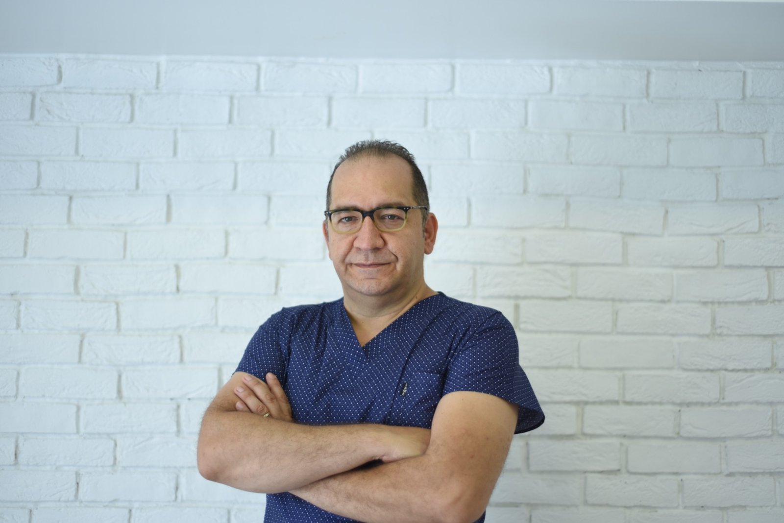 Op. Dr. Alparslan Demir, lacivert formasıyla muayenehanesinde