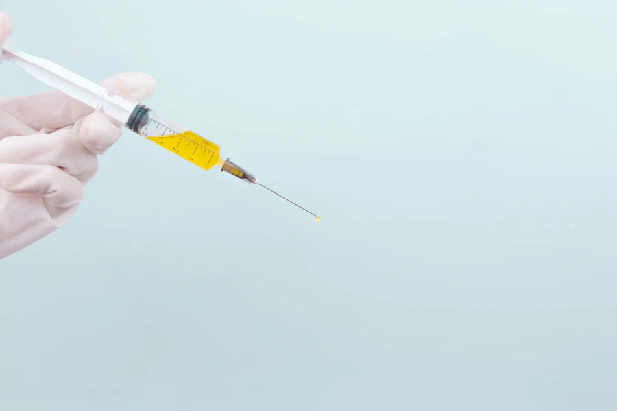 Gloved hand holding a syringe against a light blue background